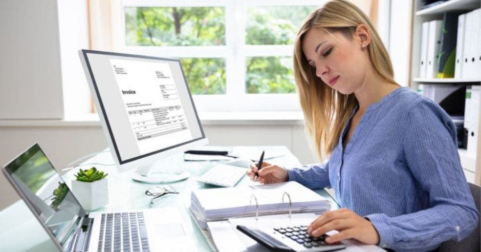 mujer joven con blusa azul, estudiando en un escritorio con una computadora