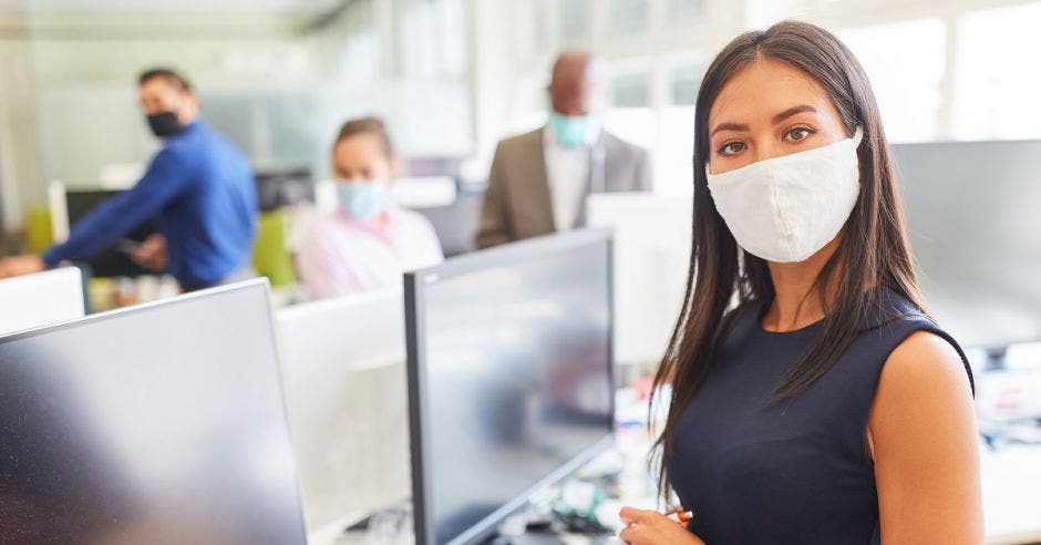 una mujer con mascarilla junto a una computadora