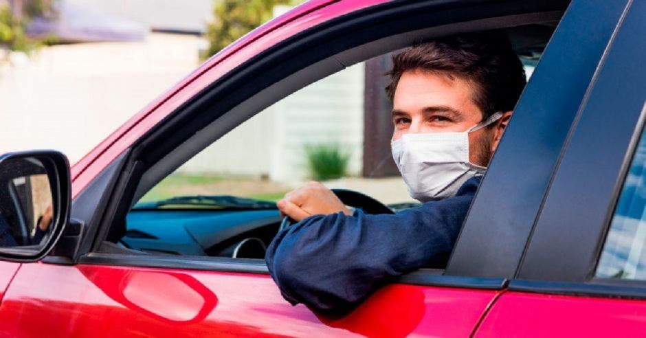 Una persona con mascarilla conduciendo un vehículo rojo