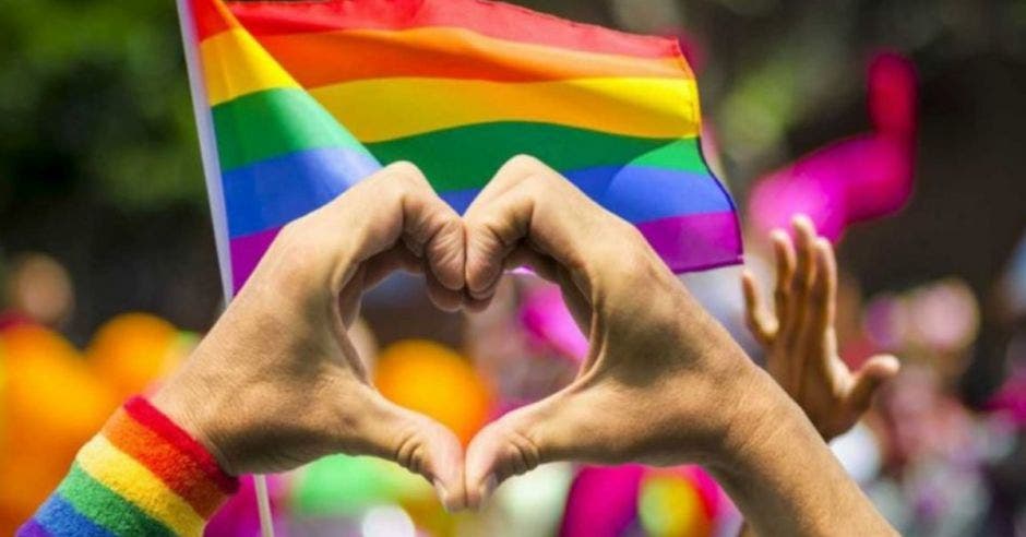 manos formando un corazón de fondo la bandera LGBT