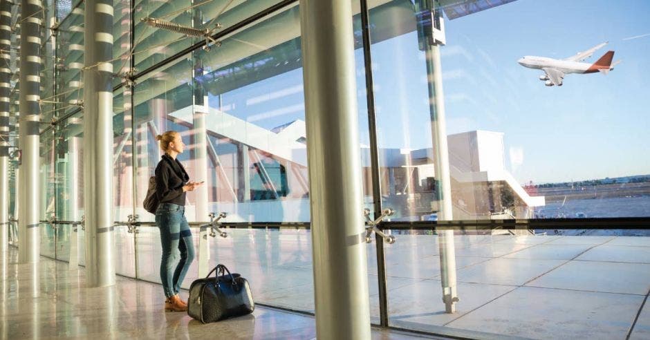 una mujer divisa un avión a través del cristal del lobby del aeropuerto