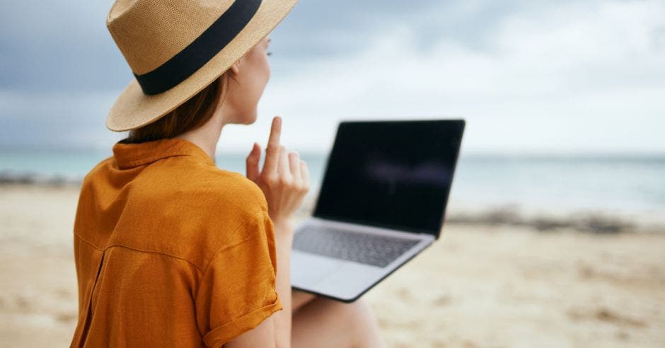 una mujer sentada en la playa con una computadora en su regazo
