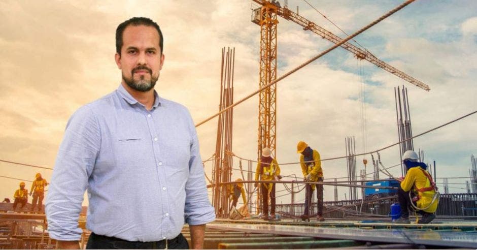 hombre con barba con camisa azul, fondo de una construcción con obreros