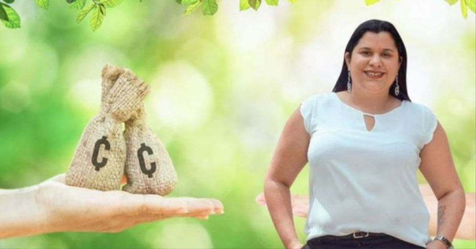 mujer de cabello negro con blusa blanca y pantalón negro, junto a dos costales con el símbolo de colones