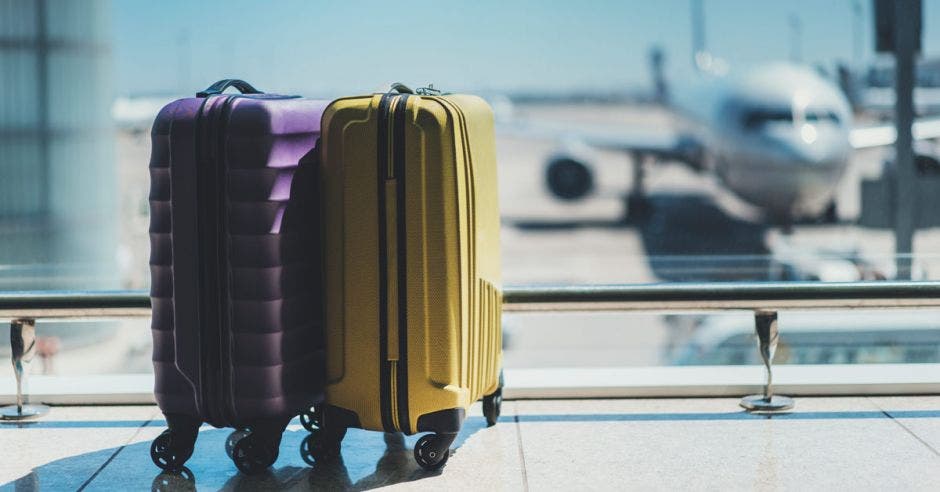 Maletas en la sala de salida del aeropuerto, avión en segundo plano, concepto de vacaciones de verano