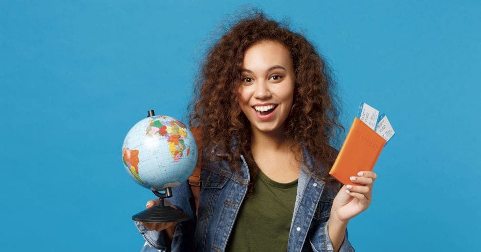 una mujer sonriente con dos boletos en la mano y un globo terráqueo