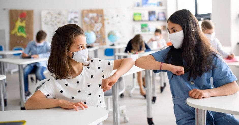 Dos menores con mascarillas saludándose con el codo