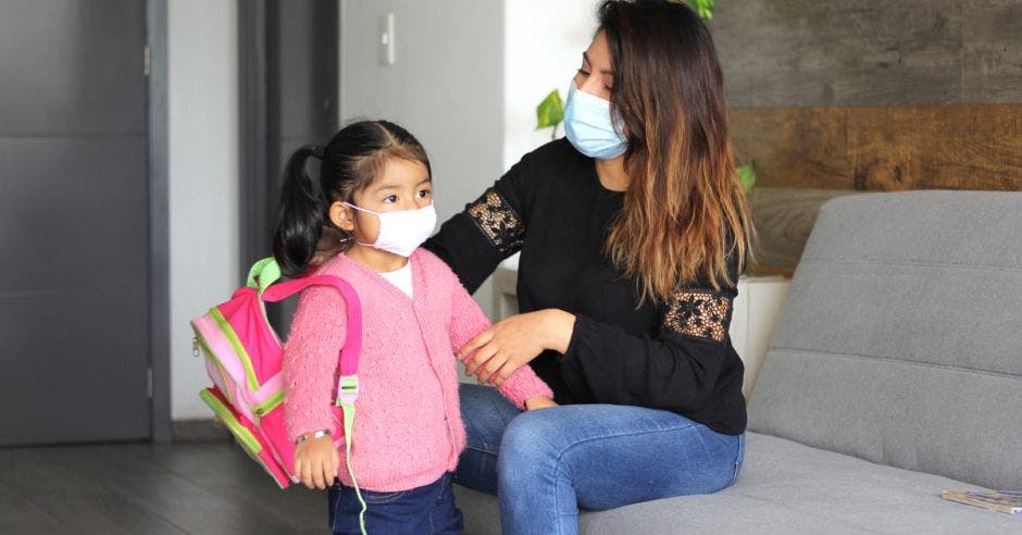 Una mujer en un sillón con su hija y un bulto escolar