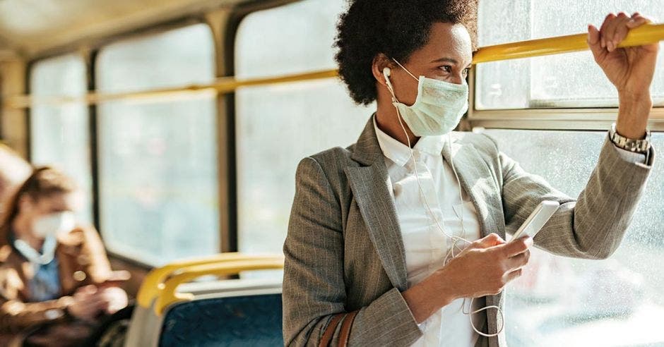 mujer de cabello negro corto con mascarilla, saco gris y camisa blanca en transporte público