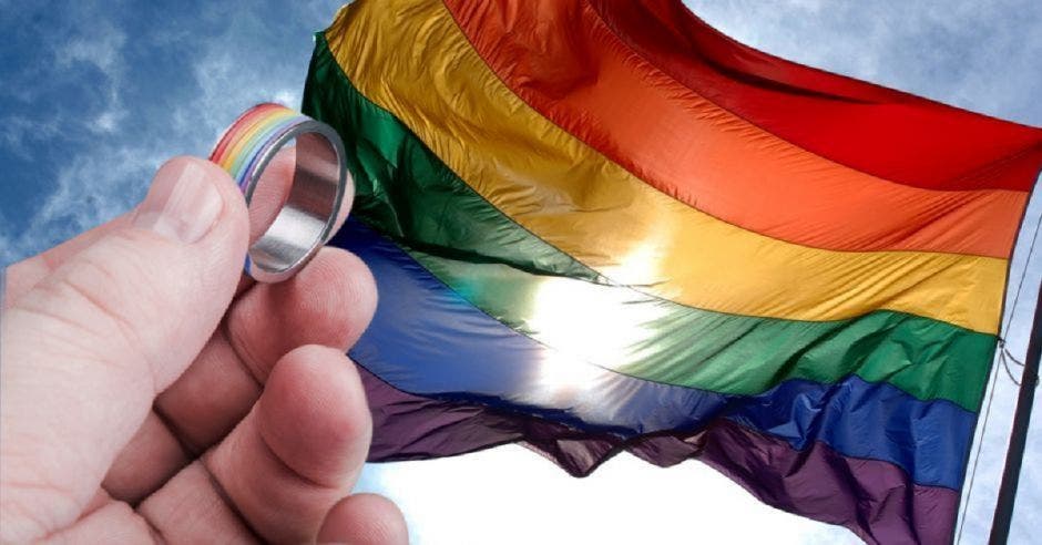 Una mano sosteniendo un anillo y una bandera del moviento LGTBI