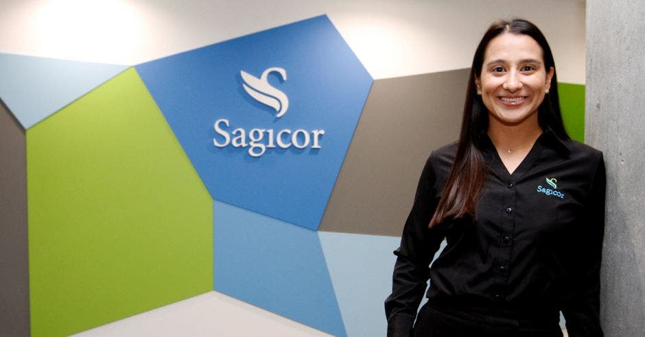 una mujer sonriente con camisa negra, posa sobre el logo en forma de cisne que dice Sagicor