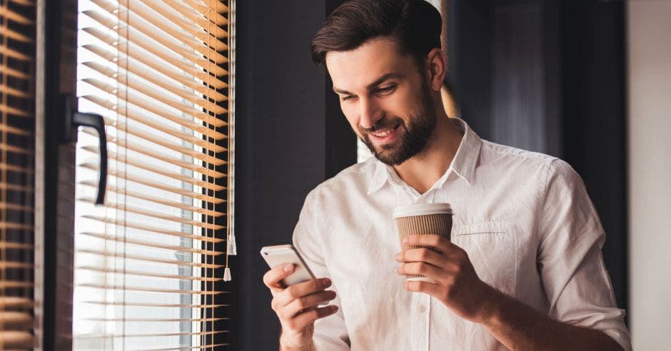 Un hombre con un celular en su mano y un café en la otra