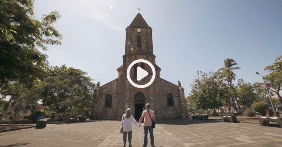 iglesia de ladrillo en un esplanada. Una pareja de adultos mayores observa la iglesia.