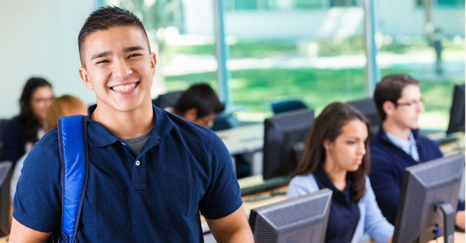 estudiante de sexto sonriendo y detrás otros estudiantes usando computadoras