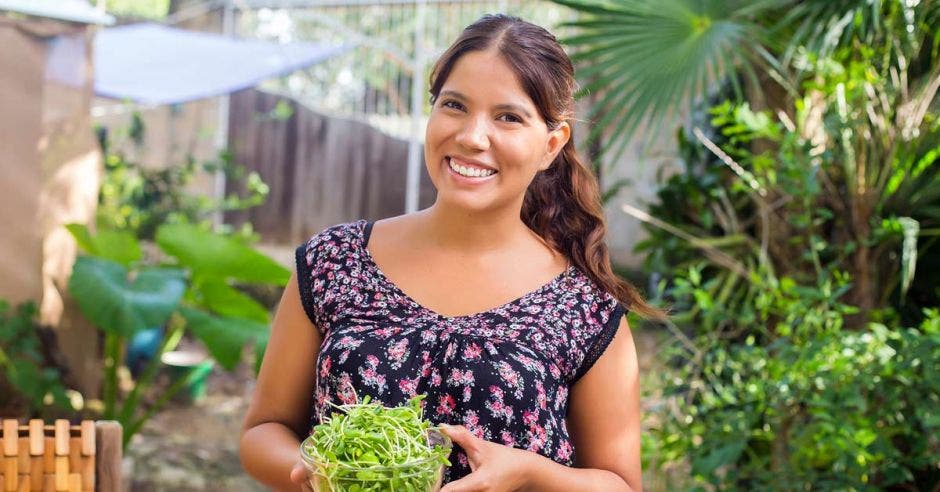 mujer con cabello castaño y blusa negra con flores sosteniendo plantas