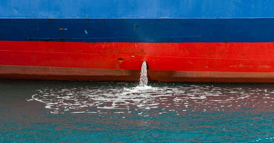 Primer plano de la bomba de achique excretando agua de un barco azul con rojo