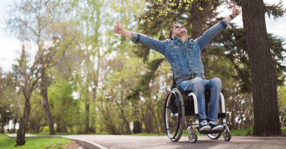 hombre en silla de ruedas levantando los brazos