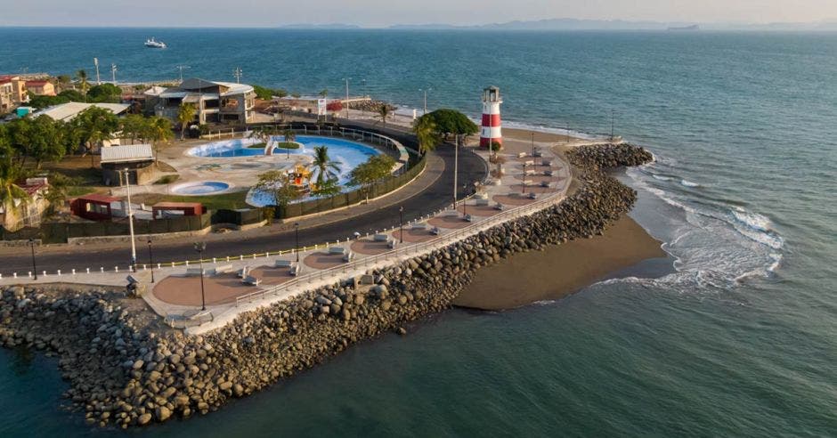 un rompeolas. El mar golpea la costa con suavidad. Un faro de rayas rojas y blancas se mira al horizonte.