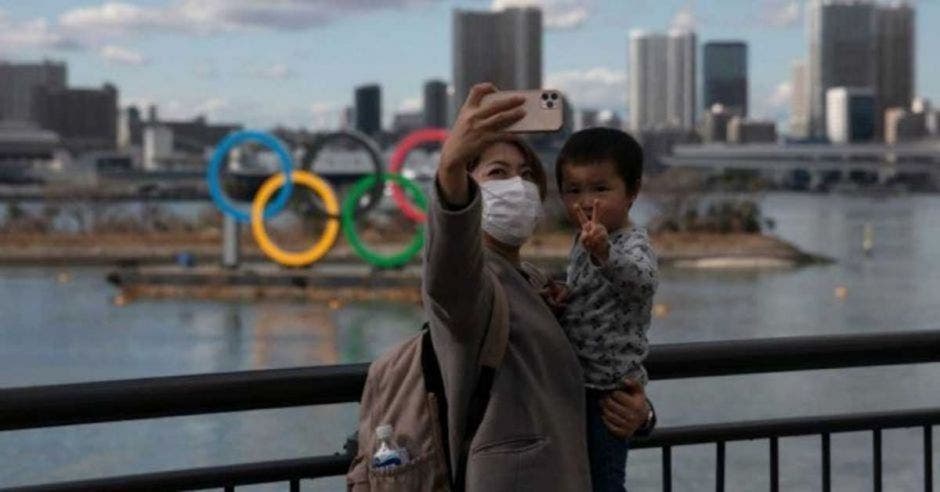 mujer y bebé tomándose selfie frente a símbolo de Juegos Olímpicos