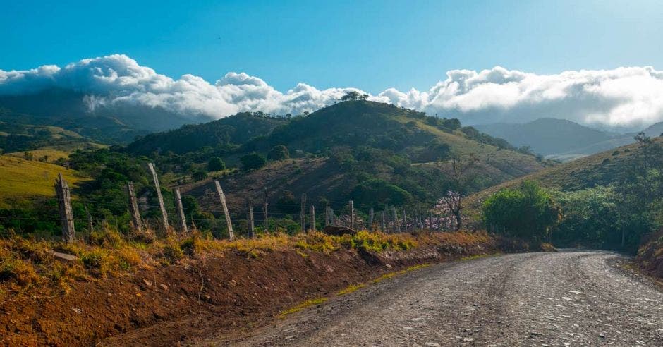 Camino de ripio rural con montañas y volcán de Tenorio (a la izquierda en las nubes) al fondo. Costa Rica