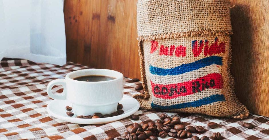 Café costarricense dentro de un saco pintado con la bandera de Costa Rica. Junto al saco, una taza de café negro.