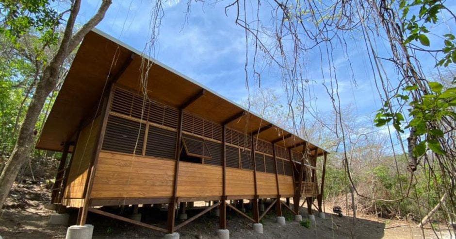 una casa de madera en medio de una bosque seco. La casa está construida sobre pilotes.