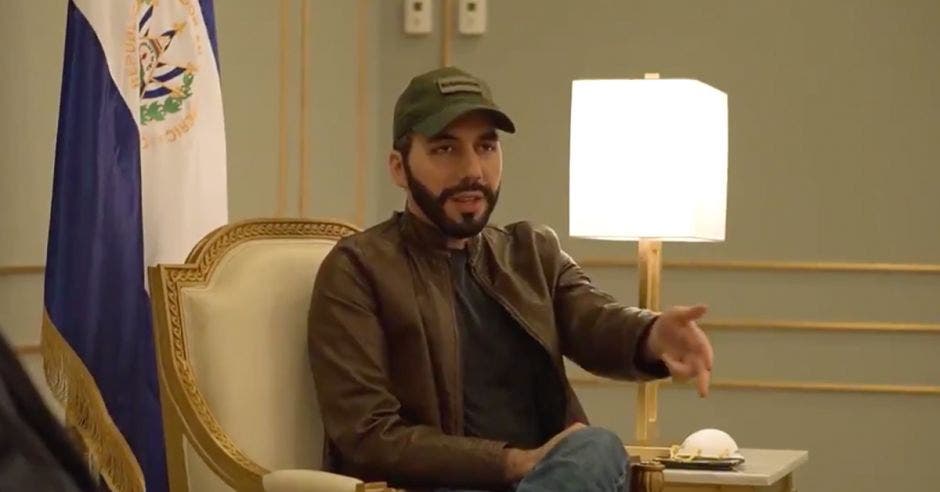 un hombre de gorra verde, barba, chaqueta café, camisa negra y jeans