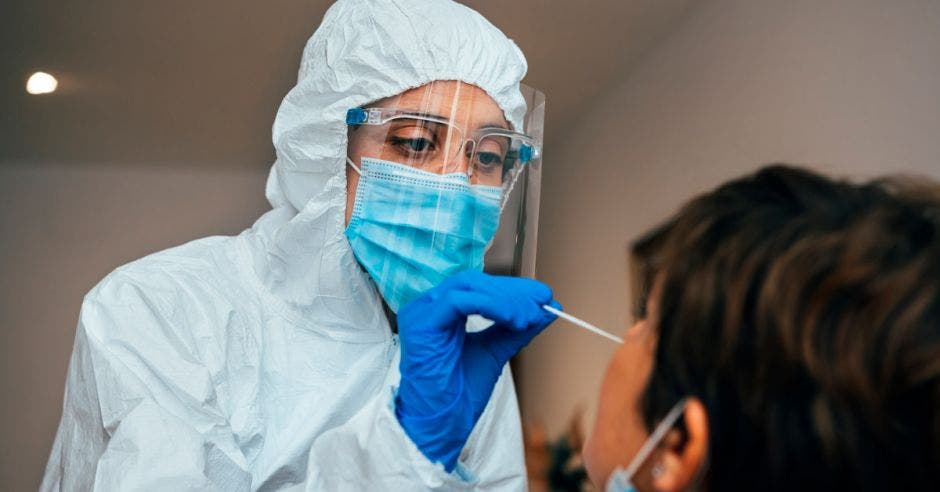 prueba rápida de antígeno realizada por una profesional de la salud vestida con kimono, careta protectora, guantes de látex y mascarilla