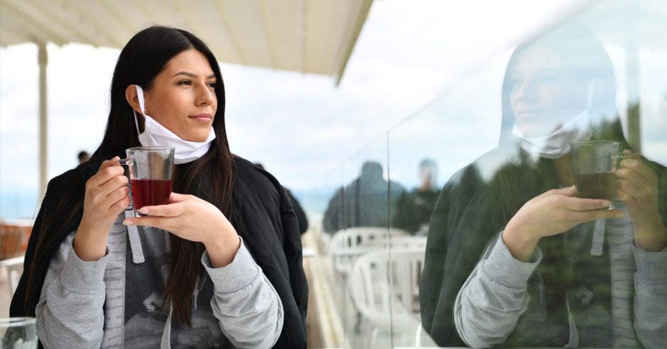 Una mujer tomando café y con una mascarilla mal puesta