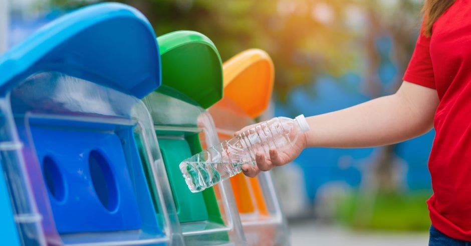 Mano de mujer de primer plano lanzando una botella de agua de plástico vacía a la papelera de reciclaje, concepto de protección del medio ambiente