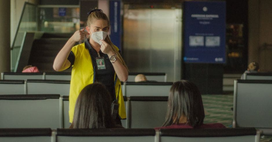 una mujer con mascarilla y chaleco amarillo le indica a dos persona una dirección