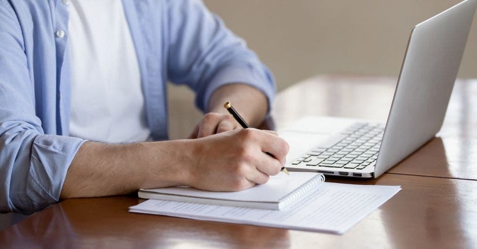 hombre tomando curso en línea y anotando en libreta