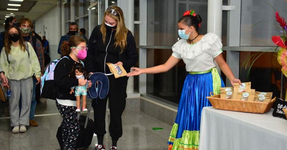 una mujer arribando al aeropuerto. La recibe una mujer de traje folclórico repartiendo panecillos.