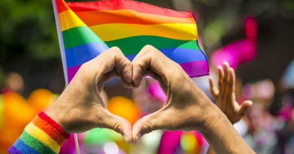 Persona haciendo corazón frente a bandera gay