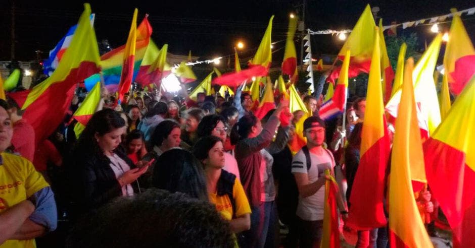 Adeptos del PAC bailan en su sede mientras esperan resultados. Banderas amarillas y rojas ondean en las calles.