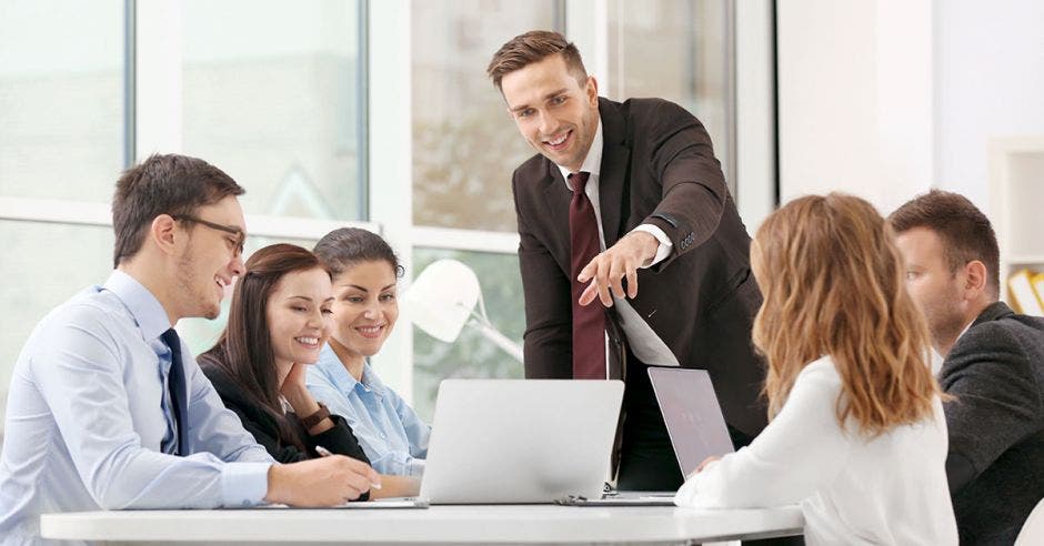 hombres y mujeres jóvenes en una reunión de trabajo viendo laptop