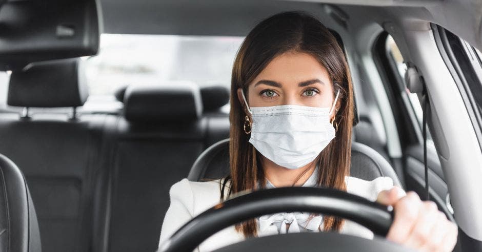 mujer joven usando mascarilla, manejando automóvil