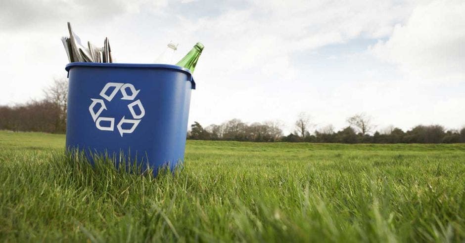 un bote de basura azul con material de reciclaje adentro, como botellas de vidrio, periódico y cartón