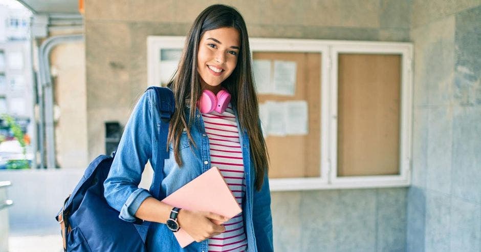 mujer joven estudiante con audífonos y libreta rosa en mano