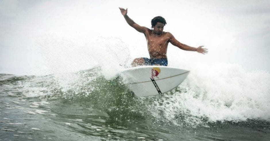 un hombre moreno surfeando con una tabla color blanco