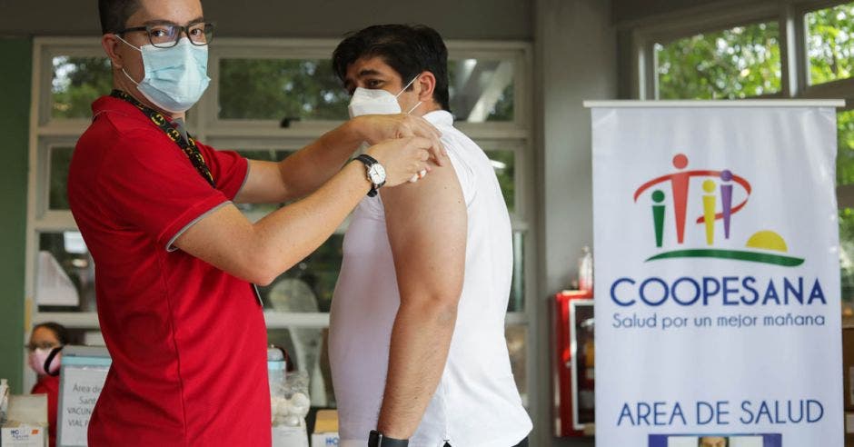 un hombre de mediana edad está siendo vacunado por hombre joven de camisa roja