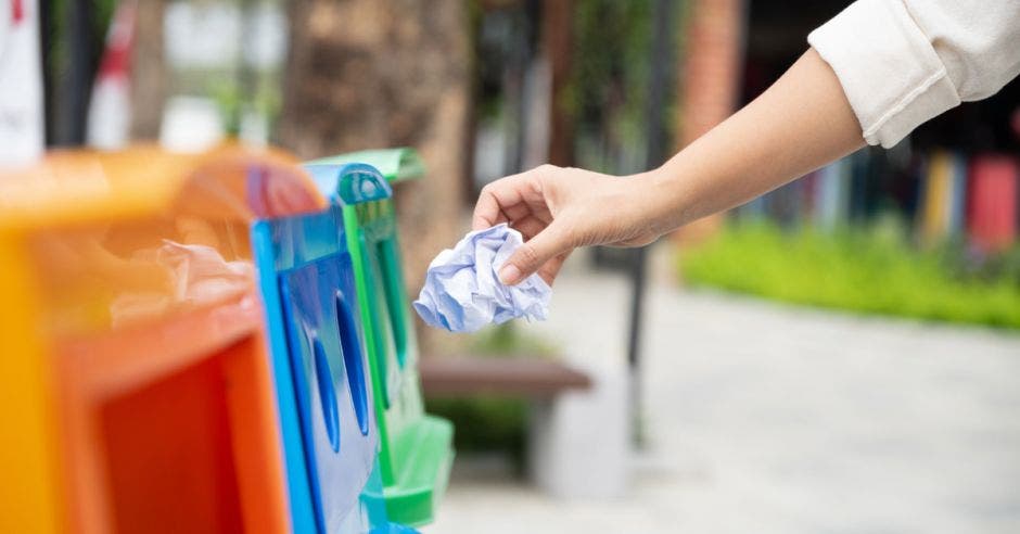 Una mujer deposita basura en contenedores de reciclaje multicolor