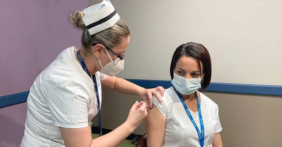 Enfermera recibiendo vacuna de otra.