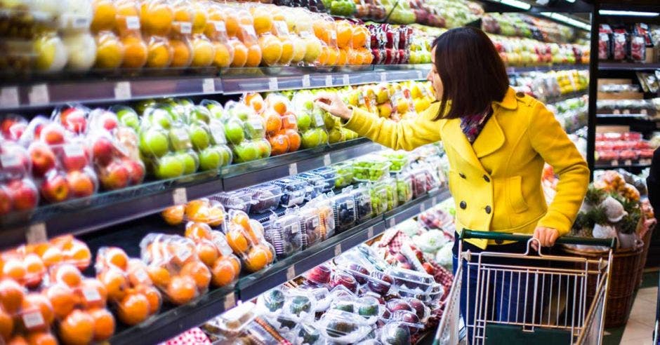 Mujer de amarillo con canasta en supermercado viendo frutas