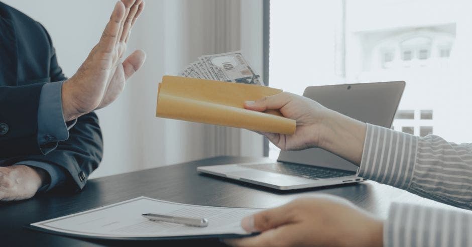 mujer ofreciendo sobre con billetes y hombre negando con la mano