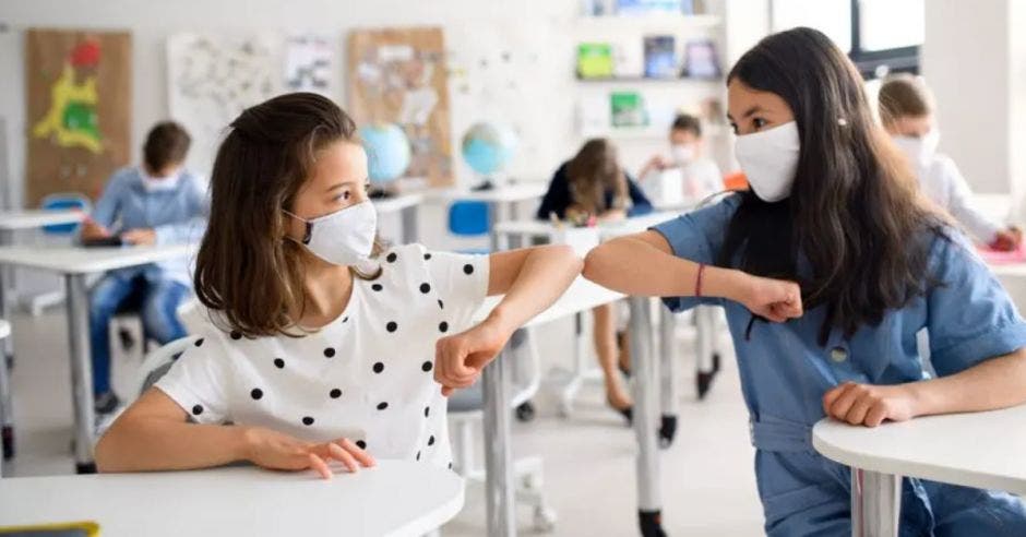 dos estudiantes en el aula pegando codo con codo, y ambas con mascarilla