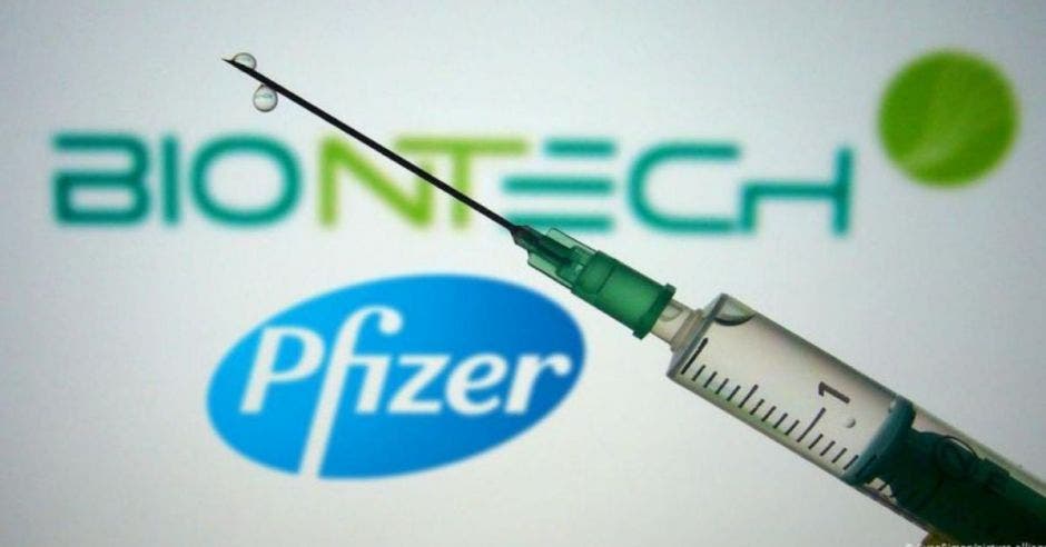 jeringa con dosis contra la Covid-19 con el logo de Pfizer al fondo