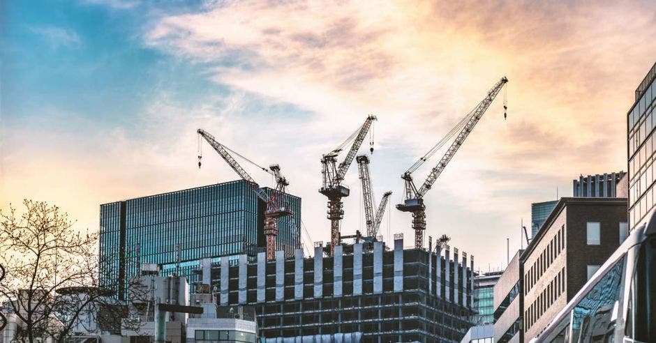 Cuatro grúas operando en la construcción de una torre de oficinas, con una tarde soleada de fondo