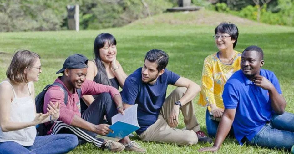 grupo de estudiantes sentados en el zacate con cuadernos y bultos