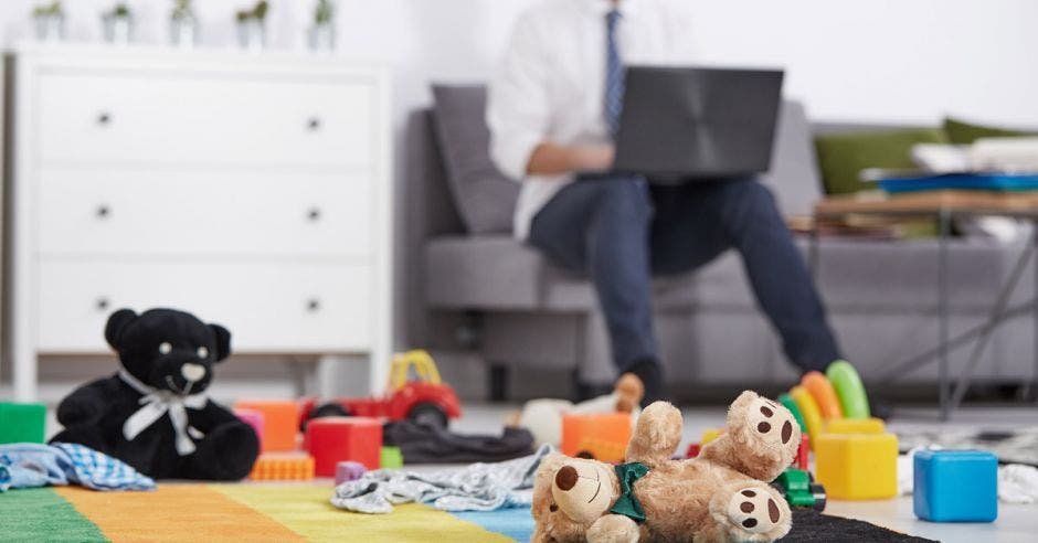 padre de familia trabajando desde la sala con juguetes en el piso